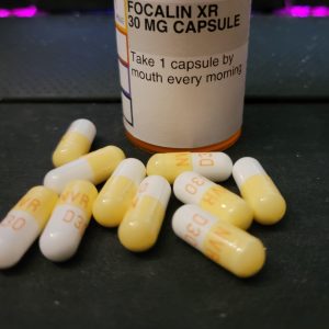 Focalin XR oral capsule in an open container with a few capsules spread on a clean surface.